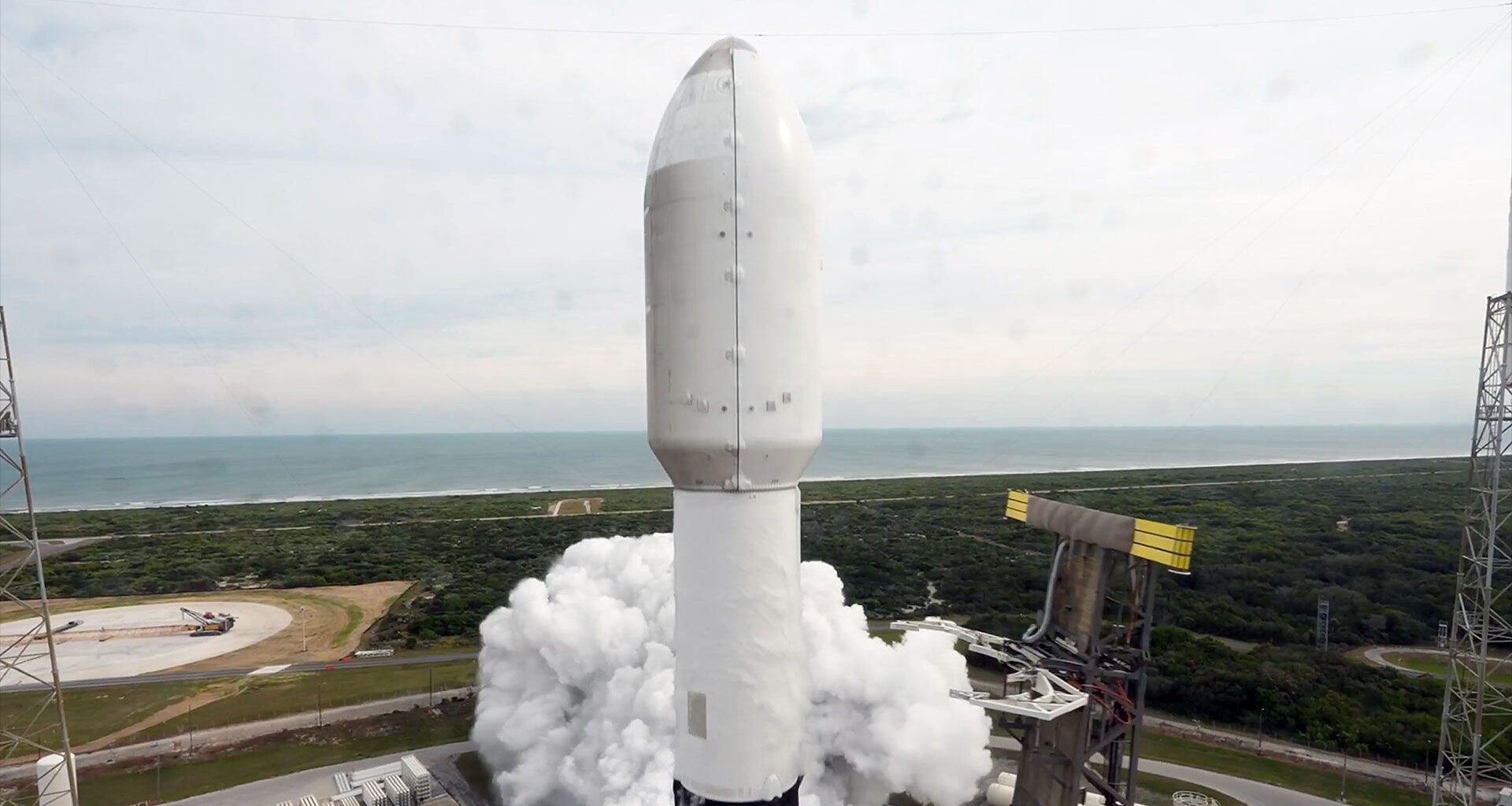 a close-up of a payload fairing atop a rocket as it lifs off from its ocean-side launch pad