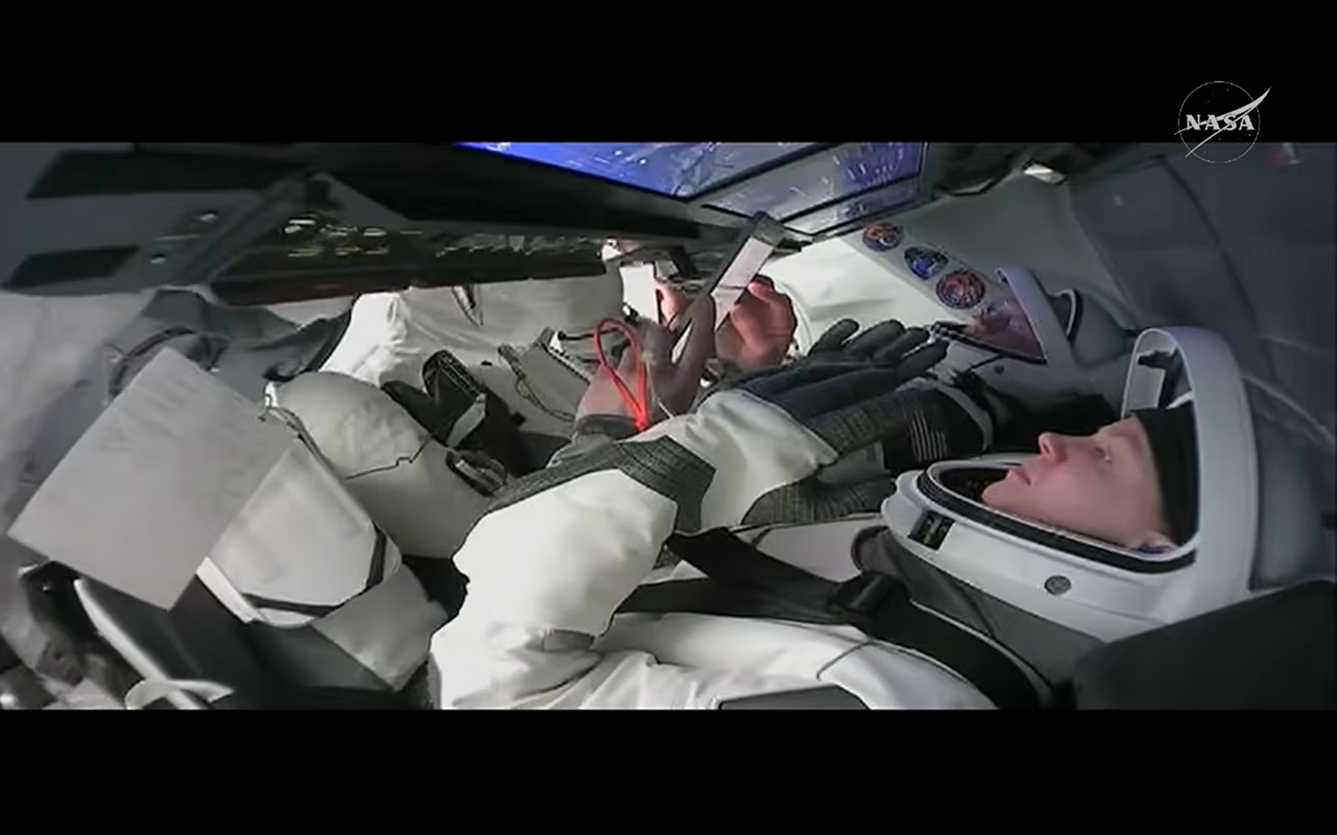 Two astronauts in white pressure suits in working on a SpaceX Crew-11 Dragon control panel