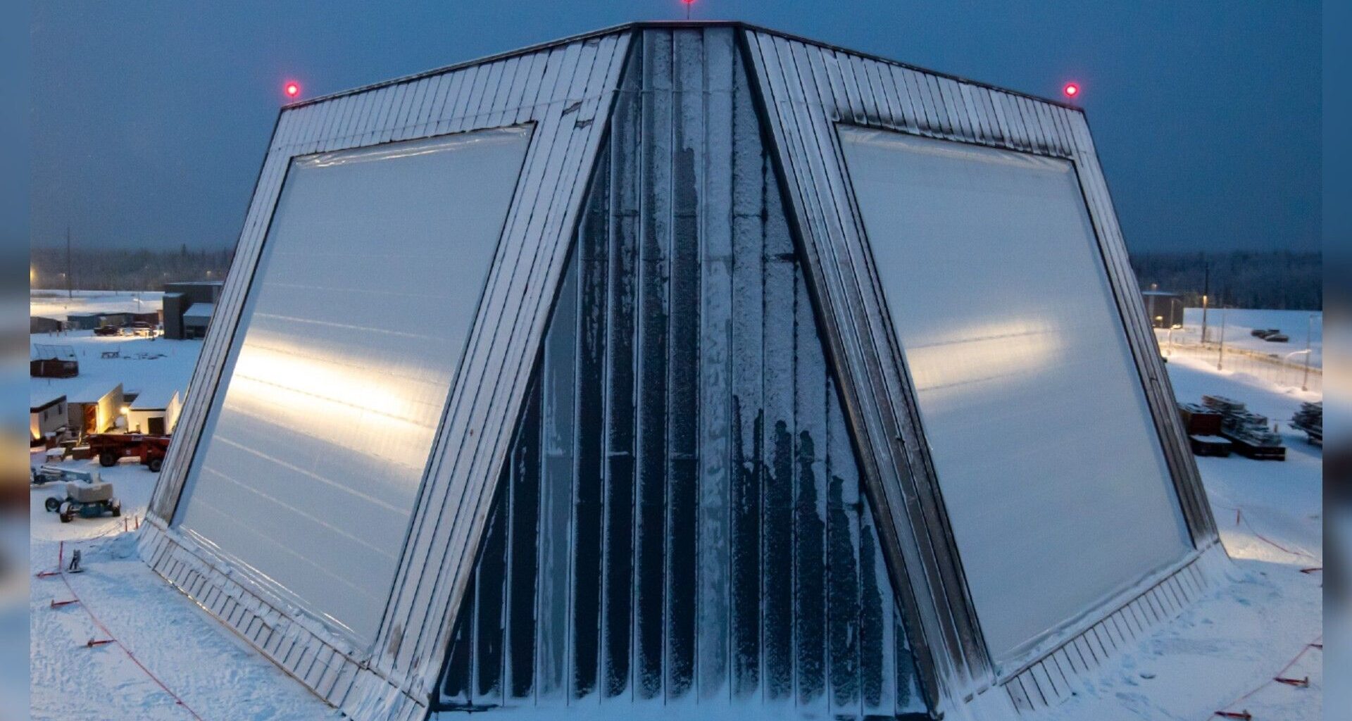 A trapezoidal building with slanted straight sides is covered in snow amidst a snowy landscape.