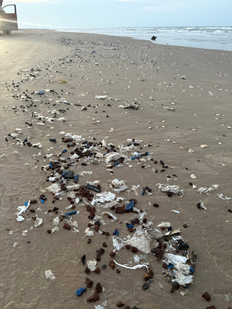Small brown, blue and white pieces of plastic scattered along a beach.