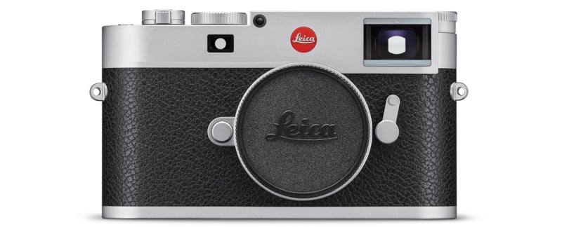 Front view of a Leica camera with a silver top, black textured body, and no lens attached. The Leica logo is visible above the lens mount and on the body cap covering the lens mount.