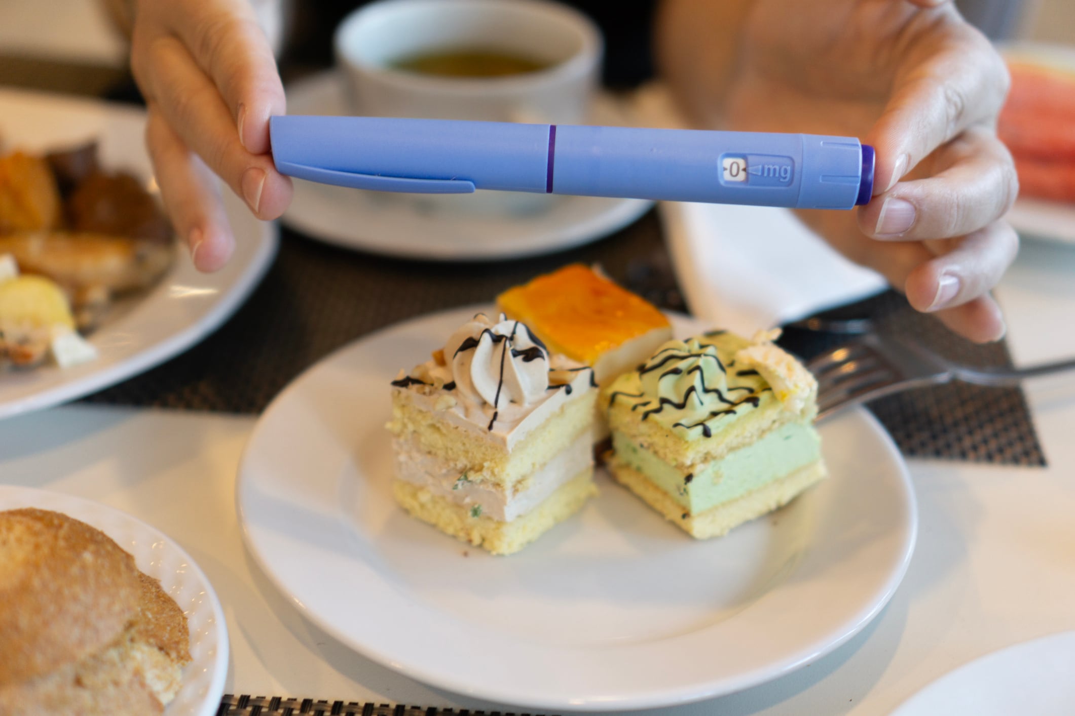 A person holding an Ozempic pen above a plate of cakes and pastries, concept of diabetes management, weight loss, and dietary choices. High quality photo