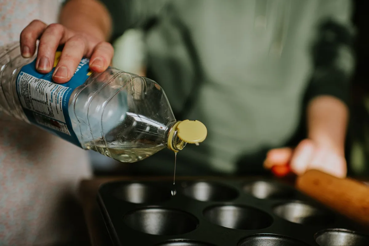 A person pours vegetable oil into a baking tray.