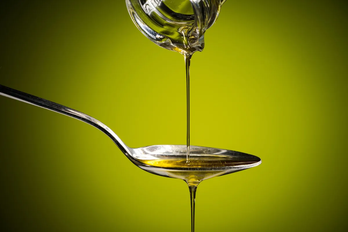 Olive oil flows from a bottle to a spoon.
