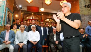 A group of people gathered indoors, with a man in a black t-shirt clapping at the front, surrounded by lanterns and a festive atmosphere.