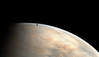 A small dark moon appears above the curved, dusty surface of a large planet against the blackness of space. The planet's surface shows tan and brown tones with subtle cloud patterns.