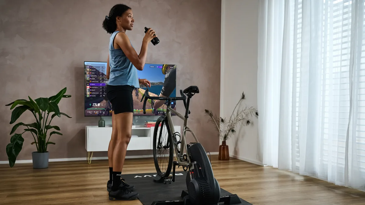 Woman standing next to indoor trainer playing Rouvy