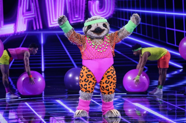 Sloth on The Masked Singer UK. The character is dressed in an 80s style workout outfit and is performing on stage