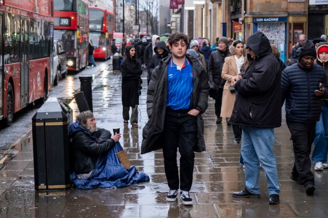 Undiscouraged by the rain, shoppers and visitors out on Oxford Street braving the bad weather from the latest storm a man sits on the pavement begging for money on 28th January 2025 in London, United Kingdom. Oxford Street is a major retail centre in the West End of the capital and is Europes busiest shopping street with around half a million daily visitors to its approximately 300 shops, the majority of which are fashion and high street clothing stores. (photo by Mike Kemp/In Pictures via Getty Images)