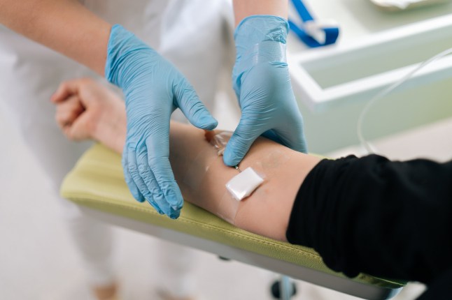 High-angle view of skilled nurse giving intravenous infusion to female patient in clinic. Medical worker in uniform inserting IV line needle in vein of woman at hospital. Medicine, vitamin therapy.