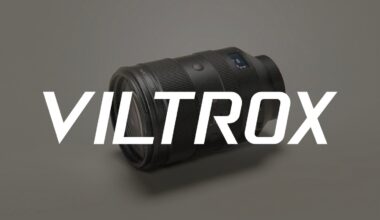 A black camera lens lies on a light gray surface with the word "VILTROX" in large, bold white letters displayed across the image.