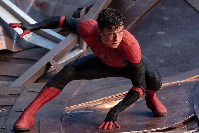 Tom Holland as Spider-Man, with his mask off but wearing the suit and landing on the ground in a pose.