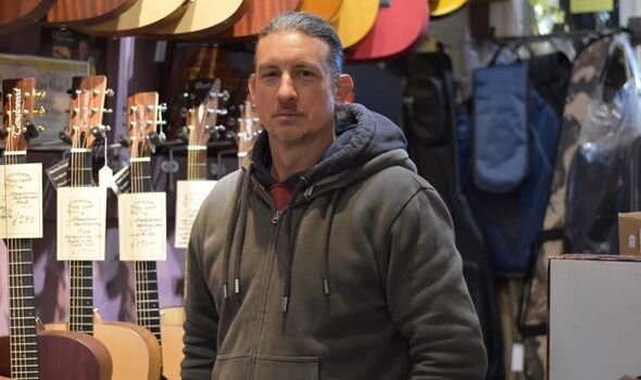 Mark White in front of guitars in his shop