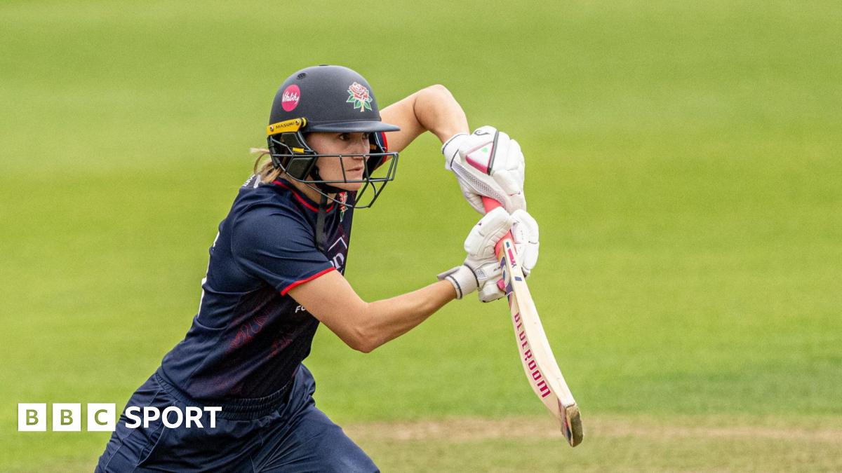 Gaby Lewis playing a shot off the front foot with her bat held high. She is wearing a navy kit with a navy helmet