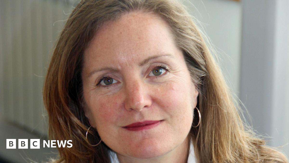 Laura Shoaf has shoulder-length light brown hair. She is wearing small hoop hearings and is slightly smiling towards the camera