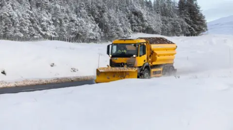 PA Media A bright yellow snowplough makes its way through heavy snowfall on the A87 road  
