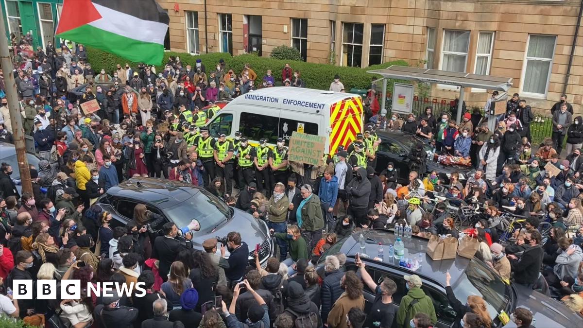 Dozens of people surround an immigration enforcement van on a city street. Several police officers stand in front of the van.