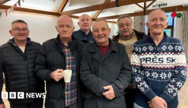 Six male veterans stand in line with arms crossed and smile at the camera.