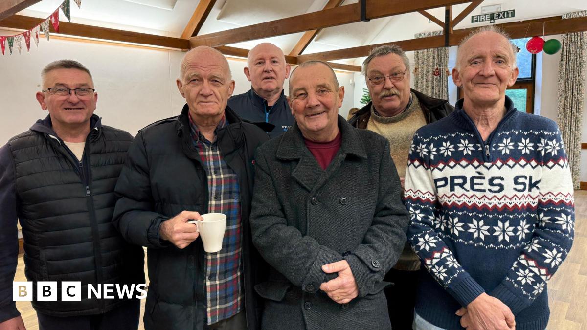 Six male veterans stand in line with arms crossed and smile at the camera.