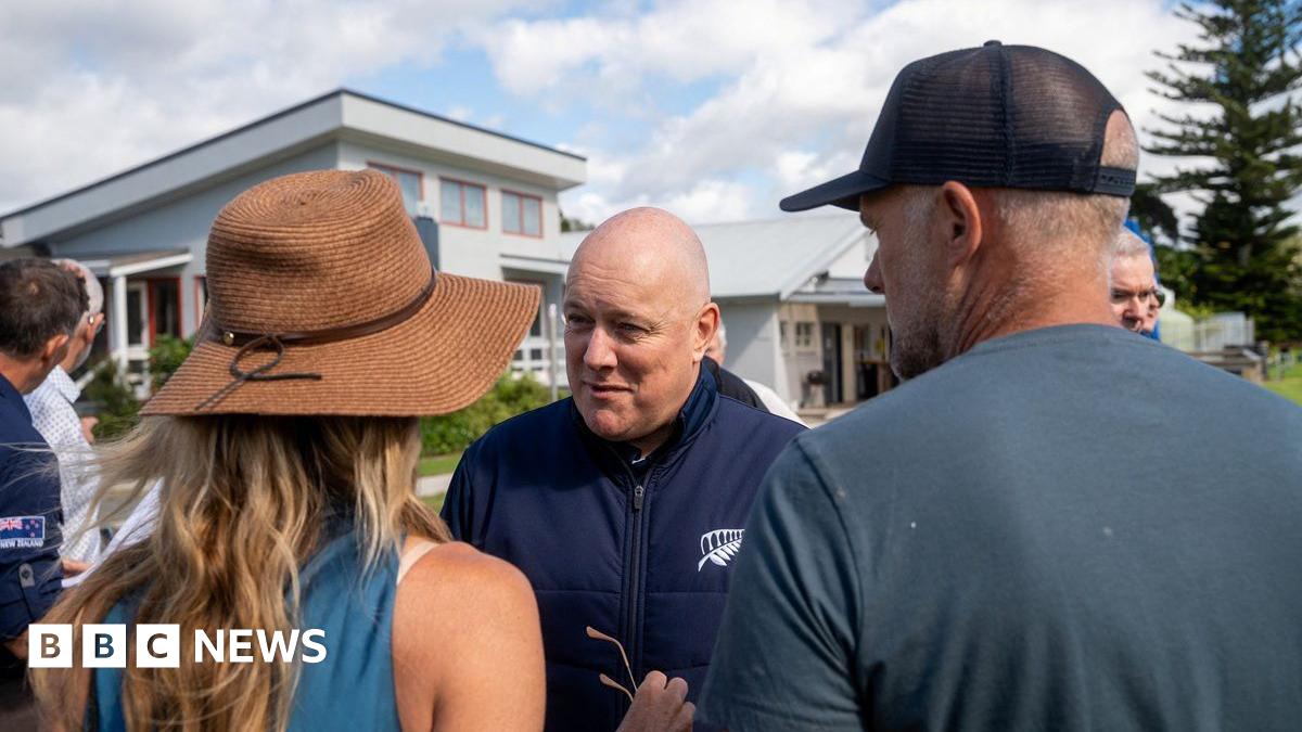 Luxon in a navy zip-up jacket speaking to a man and woman