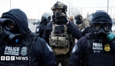 Law enforcement officials wearing heavy military gear and gas masks stand guard during a protest in Minneapolis, Minnesota.