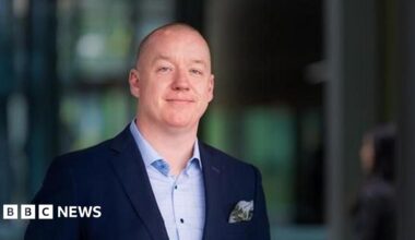 Professor Ken Sloan is seen in an official photograph. He is wearing a light blue shirt and navy jacket and the background is blurred.