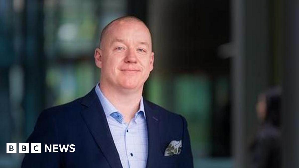 Professor Ken Sloan is seen in an official photograph. He is wearing a light blue shirt and navy jacket and the background is blurred.