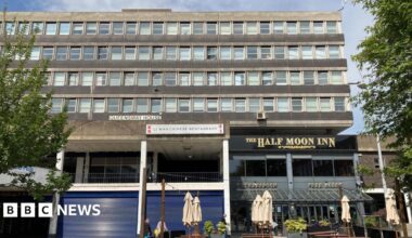 West Precinct is a large, concrete Brutalist-style building. Pictured are two businesses at the base of the block - the Half Moon Inn and a Chinese restaurant with its blue shutters down.