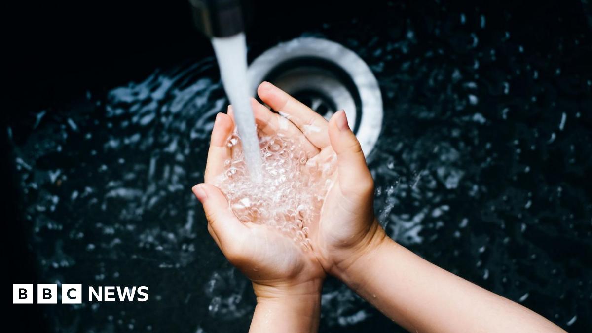 A young woman's hands cup water as it runs from a tap into a deep black sink.