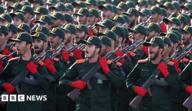 Iranian Revolutionary Guard Corps (IRGC) soldiers march in formation in September 2024. The group of men wear matching green and red uniforms and hold rifles