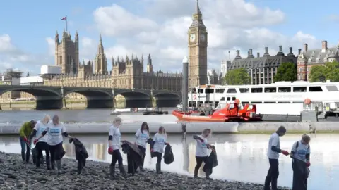 Getty London Aquarium staff clean up bank of South Bank with Parliament behind them