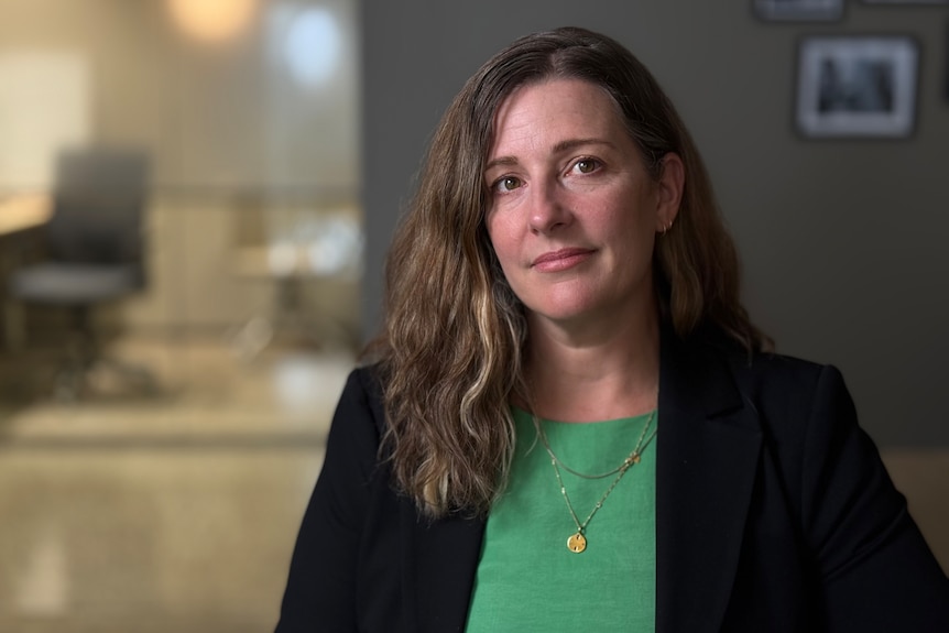 A head and shoulders portrait of a smiling woman wearing a green shirt and black blazer.