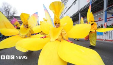 Performers in bright yellow floral costumes pose on the parade route.