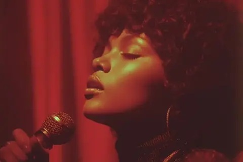 Sienna Rose Sienna Rose in another image with eyes closed and a microphone in front of her, with her dark hair and large hoops and face seen in profile 