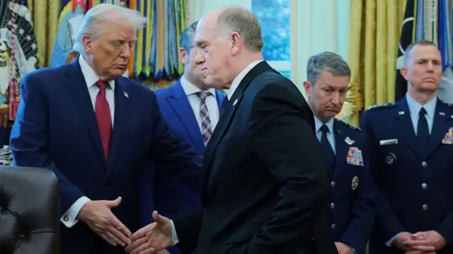 Donald Trump (L) shakes hands with Tom Homan (R) during an award ceremony in the Oval Office. Behind them, partially covered are Secretary of Defense Pete Hegseth and members of the military