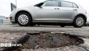Grey car drives past pothole on a road
