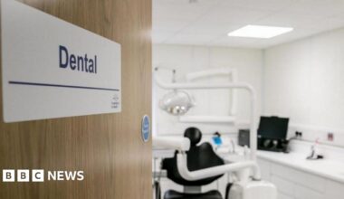 A stock image of a dentist's studio. A door with a signs saying 'dental' opens to a studio with a dentist chair and equipment in the blurred background.