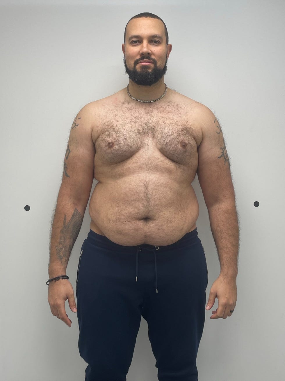 standing overweight male with torso visible wearing dark sweatpants in a neutral background