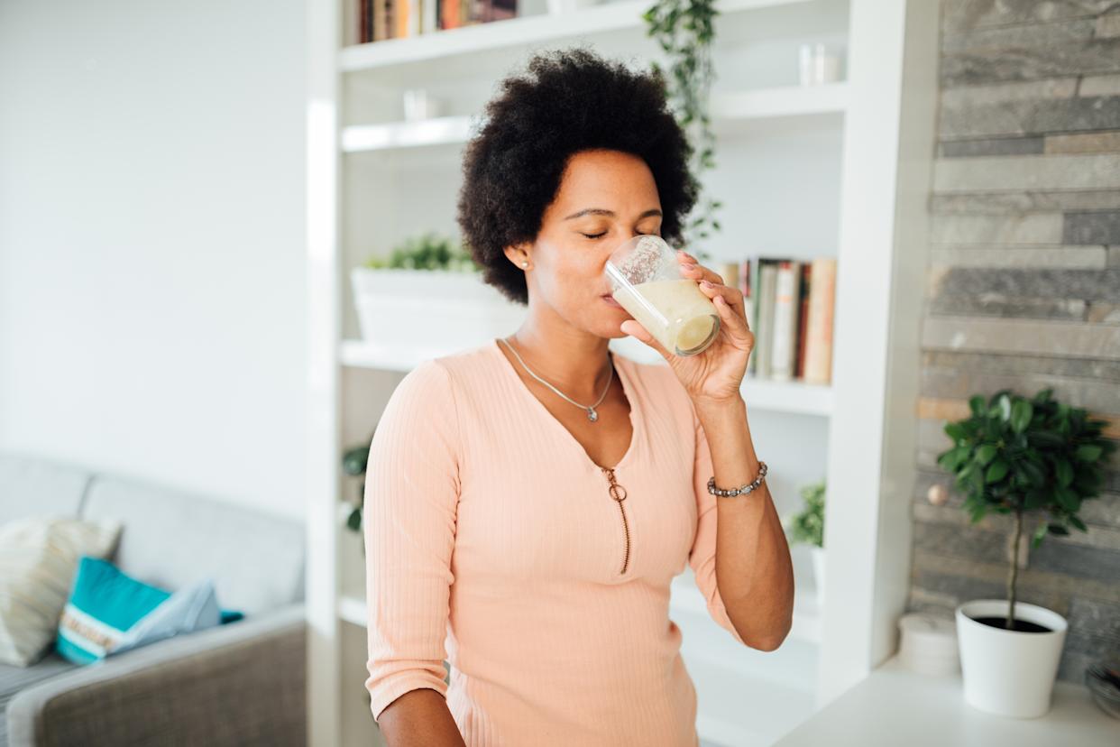 Cheerful African American woman having a healthy breakfast at home, making a shake out of different kinds of fruits