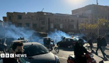 A street-view image of Iranian shopkeepers and traders protesting on motorbikes and on foot in between cars with tear gas is visible.