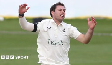 Mikey Cohen raises his hands after bowling for Kent, dressed in cricket whites and a black armband