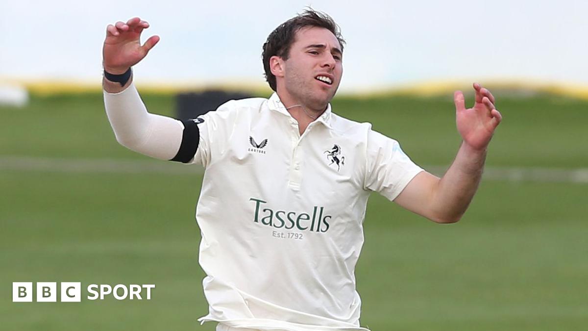 Mikey Cohen raises his hands after bowling for Kent, dressed in cricket whites and a black armband