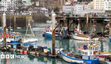 Fish Quay St Peter Port is filled with small fishing boats moored at pontoons in the harbour. Houses are close to the the harbourside.