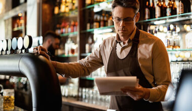 Pub landlord reading inventory behind bar