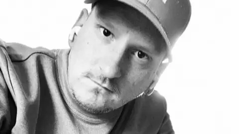 Family handout A black-and-white photo of a man wearing a cap and a top looking into to the camera. He is wearing white earbuds
