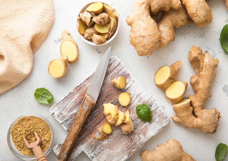 Raw fresh ginger root slices chopped with knife on wooden board with ginger powder on background.