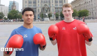Odel Kamara and Callum Makin posing with their boxing gloves. Odel has short curly, dark hair and is wearing a blue top, and Callim has short light-brown hair and is wearing a red top.