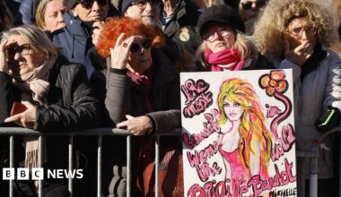 Crowds gather for the funeral of French film icon Brigitte Bardot in Saint-Tropez, southern France. One woman is seen holding a picture of the actress. Photo: 7 January 2026