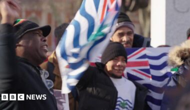A group of people protest in central London. Some are holding the flag of the British Indian Ocean Territory.