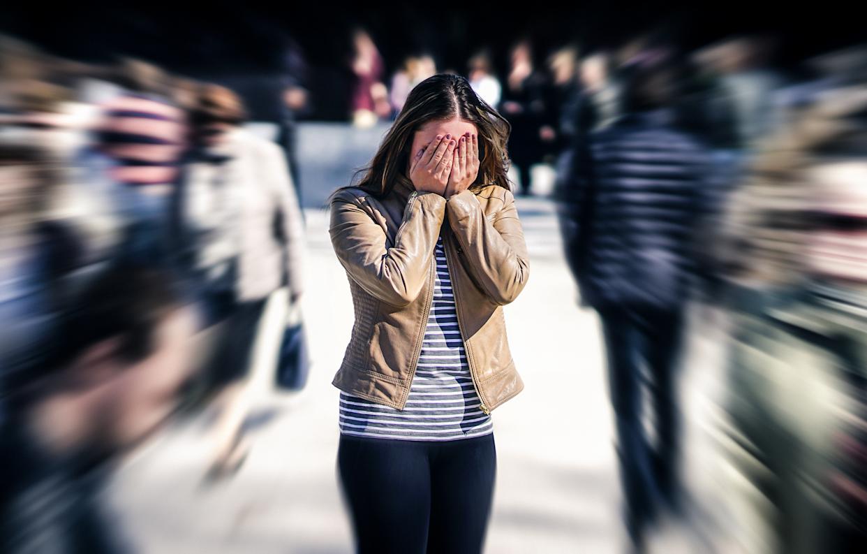 Shot of a woman with her hands over her face in distress amongst a crowd of people